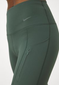 Høytlivs, olivengrønne leggings med en jevn tekstur. Har en liten glidelåslomme og en subtil grå logo på midjen.