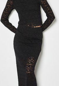 Schwarzes Spitzen-Zweiteiler-Outfit mit langärmeligem Crop-Top und hoch tailliertem Rock, der ein durchsichtiges florales Spitzenmuster und gewellte Kanten zeigt.