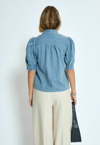 Jeansblus med vertikala vita ränder, puffiga kortärmade ärmar och en spetsig krage, i kombination med ljusfärgade veckade byxor.