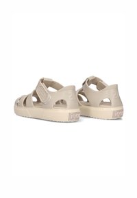 Beige plastic sandals with open design, featuring a strap with Velcro closure and textured soles. Logo and number detail on heel.
