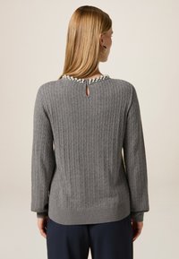 Grijze gebreide trui met een ribbelstructuur, parelaccenten bij de halslijn en een sleutelgatopening aan de achterkant. Lange mouwen en een relaxte pasvorm.