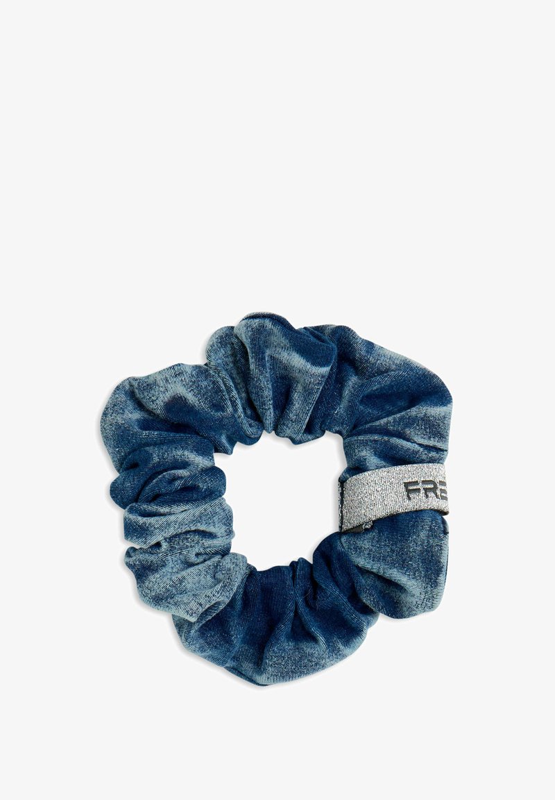 Chouchou en velours bleu avec un tissu froncé et une petite étiquette en argent comportant un texte noir partiel sur fond blanc.