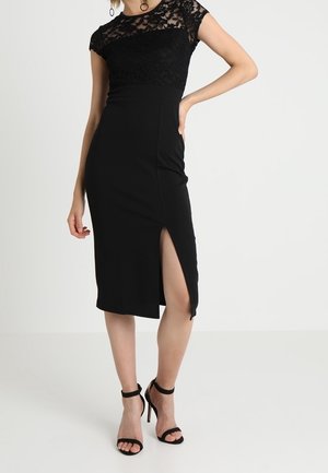 Schwarzes Kleid mit Spitze am Oberteil, kurzen Ärmeln und figurbetonter Silhouette. Verfügt über einen hohen Beinschlitz und glatten Stoff. Kombiniert mit schwarzen Sandalen mit Absatz.