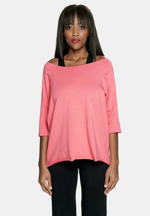 Luźna bluzka off-the-shoulder w pastelowym różu z bawełny, z rękawami o długości trzech czwartej, połączona z czarnymi spodniami, prosty design, miękka tekstura.