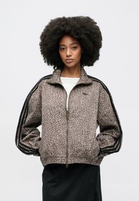 Καφέ μπουφάν με φερμουάρ και σχέδιο, με ψηλό γιακά, μαύρες ρίγες στα μανίκια και ριμπ τελείωμα, συνδυασμένο με μαύρη φούστα.