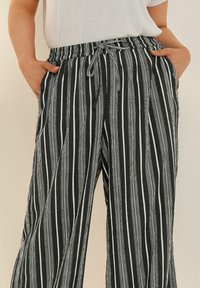 Svart- och vitrandiga byxor med elastisk midja och justerbar snörning. Lätt vikt, löst passform och sidofickor. Vertikalt randmönster.