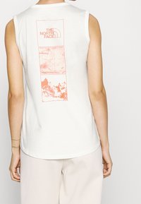 Top bianco senza maniche con grafica color salmone: logo The North Face, mappa topografica e paesaggio montano sul retro.