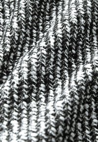 Tissu tricoté en noir et blanc avec un motif texturé ; des rayures alternant entre fines et épaisses créent une apparence dimensionnelle.