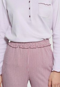 Maglia a maniche lunghe viola chiaro con bottoni e tasca, abbinata a pantaloni a righe rosse e bianche con vita arricciata.