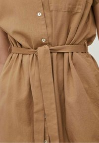 Robe en lin marron avec un devant à boutons, manches courtes et ceinture assortie en tissu, présentant une texture douce et une taille cintrée.