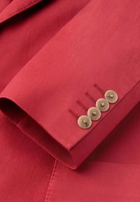 Sleeve of red textured blazer featuring four beige buttons arranged vertically near the cuff.