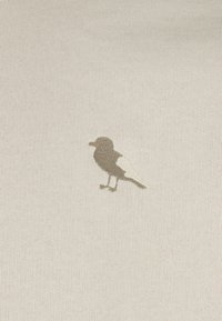 Helles beiges Gewebe mit einer stickten Vogelsilhouette in Dunkelbraun und einem weißen Flügel, das ein strukturiertes Strickmuster zeigt.