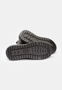 Chaussures en caoutchouc noir avec un motif de semelle texturé. Présentent de profonds canyons pour l'adhérence et des bords renforcés pour la durabilité.