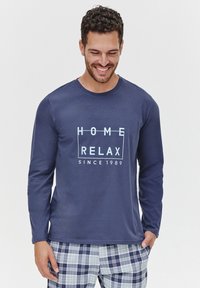 Granatowa koszula z długim rękawem z białym napisem "HOME RELAX SINCE 1989", w zestawie z długimi spodniami piżamowymi w kratkę w jasnym niebieskim i białym kolorze.