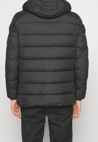 Sort dunjakke med vandret quiltning, en hætte og ribbede manchetter. Blød tekstur med en glat finish, med en afslappet pasform.