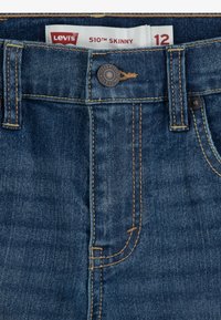 Tamno plave traperice s uskim krojem. Sadrže kontrastnu žutu šavovu, petlje za remen i metalnu dugmad na struku. Etiketa nosi natpis "Levi's 510 Skinny."