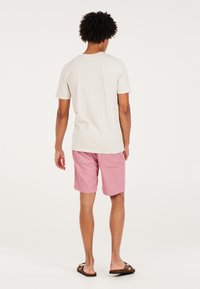 Lyse beige bomulds t-shirt med korte ærmer, parret med lyserøde stribede shorts. Bæres med brune flip-flops. Bagfra, ensfarvet baggrund.