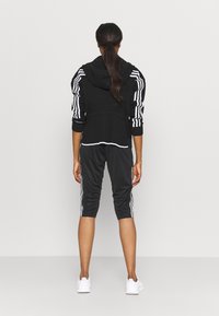 Svart atletisk hoodie med vita ränder på ärmarna, tillsammans med svarta cropped byxor med vita sidosträngar. Vita sneakers fulländar outfiten.