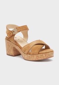 Tan kleurige suède platform sandalen met een kurken blokhak, kruisende banden en een verstelbare enkelband met een goudkleurige gespsluiting.