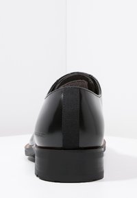 Chaussure de costume en cuir noir avec une finition lisse et brillante, dotée d'un maintien élastique au talon et d'une semelle robuste en caoutchouc noir. Design simple et classique.