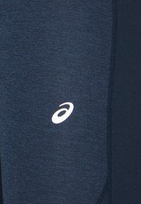 Leggings sportivi blu navy con texture melange, cuciture piatte e un logo riflettente sulla coscia. Materiale morbido e elasticizzato.