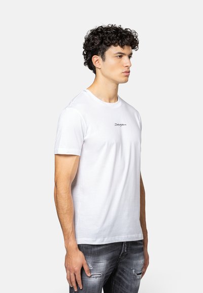 Witte katoenen t-shirt met een ronde hals, korte mouwen en een klein zwart geborduurd logo op de borst. Model draagt grijze distressed jeans.