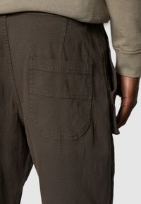 Ciemnozielone spodnie cargo z dużą boczną kieszenią i przeszyciami, wykonane z fakturowanego materiału. Talia jest delikatnie elastyczna.