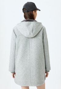 Cappotto in misto lana grigio con cappuccio, dalla vestibilità rilassata e maniche lunghe. Texture liscia e design semplice senza accenti aggiuntivi.