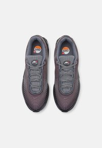Un paio di sneakers Nike Air Max grigio scuro e viola con lacci grigi e upper in mesh a motivo, viste dall'alto su uno sfondo bianco.