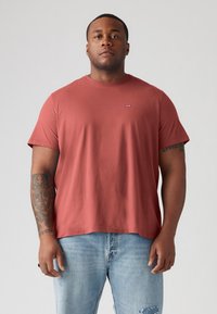 Rode katoenen t-shirt met korte mouwen, ronde hals en klein logo op de borst, gecombineerd met lichtblauwe versleten jeans.