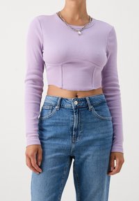 Top corto de manga larga en un tono púrpura claro, hecho de tela de canalé, combinado con jeans de mezclilla azul de cintura alta con cierre de botón y bolsillos.