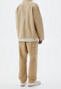 Lyse beige jakke med løstsiddende pasform og glat tekstur samt krave, der kan foldes ned, kombineret med matchende, tilspidsede cargobukser og hvide sneakers.