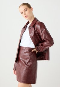 Bordeaux faux leren jack met een kraag en twee knopen, gecombineerd met een bijpassende strakke minirok, beiden met een gestructureerde afwerking.