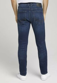 Jeans de mezclilla azul oscuro con corte ajustado, que cuentan con bolsillos traseros con costuras distintivas y una etiqueta de cuero en la pretina.