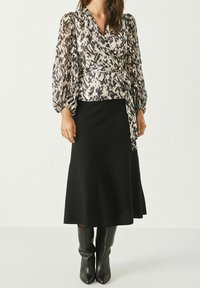 Langarm wikkelblouse in een multikleurig abstract patroon, gecombineerd met een zwarte midi-rok en kniehoge zwarte laarzen. Glad materiaal, getailleerde pasvorm.