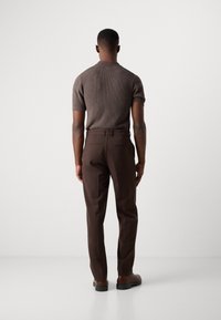 Chemise en tricot marron à manches courtes avec un motif texturé, associée à un pantalon sur mesure marron foncé. Fini lisse et coupe structurée.