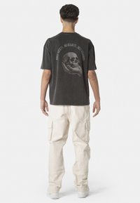 Grey graphic t-shirt with skull design on the back, worn with cream cargo pants. Features short sleeves and a relaxed fit.