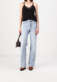 Camisole noire à bordure en dentelle, jean bleu clair à jambes droites, bottines marron à talons, petit sac à main marron. Design simple et contemporain.