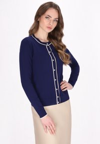 Cardigan albastru marin cu bordo crem și accente de butoane. Are mâneci lungi, guler rotund și o siluetă ajustată. Textură tricotată plană.