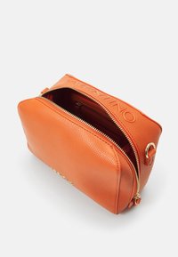 Borsa in pelle arancione con texture granulosa, ferrature dorate, chiusura con zip e logo in rilievo sulla tracolla. Aperta, mostrando i scomparti interni.