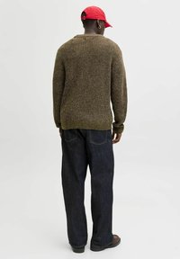 Rudas tekstūruotas megztinis su briaunotomis rankovėmis ir apačia, derinamas su laisvomis tamsiomis džinsomis ir raudonu kepurėle.