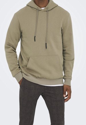 Felpa con cappuccio verde oliva in tessuto morbido, con tasca frontale, coulisse e polsini e orlo a coste. Abbinata a pantaloni scuri a quadri.