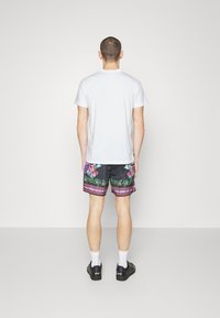 Vit bomull t-shirt och svarta badshorts med en floral design i rosa och grönt med horisontella ränder, tillsammans med svarta skor.