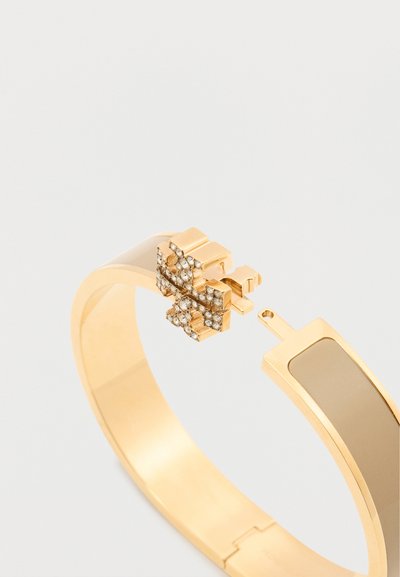 Χρυσό βραχιόλι με κλείσιμο τύπου μενταγιόν που διαθέτει σχέδιο σε σχήμα σταυρού, διακοσμημένο με μικρούς διάφανους κρυστάλλους.