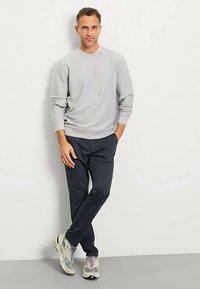 Graues Sweatshirt mit Rundhalsausschnitt, kombiniert mit marineblauen Jogginghosen. Das Model trägt graue und weiße Sneaker und steht vor einem schlichten Hintergrund.
