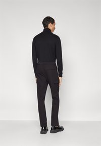 Jersey de cuello alto negro, de manga larga, con diseño ajustado. Combina con pantalones cargo negros que tienen bolsillos laterales y corte recto. Zapatos negros.
