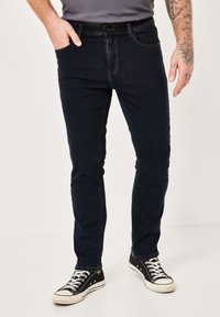 Dark denim jeans with a slim fit, featuring front pockets, subtle stitching details, and worn black sneakers with white accents.