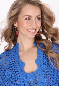 Niebieski wydziergany top z kwiatowymi akcentami i otwartym, dzierganym wzorem, uzupełniony dużymi różowymi kolczykami z koralików.