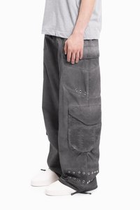 Osoba ubrana w luźne, ciemnoszare spodnie cargo z metalowymi oczkami i dużymi kieszeniami, w zestawieniu z jasnoszarym t-shirtem i białymi trampkami.