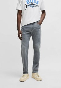 Ljusgrå denimjeans med rak passform, femficksdesign och kontrastsöm, kombinerade med en vit t-shirt med tryck och beige sneakers.